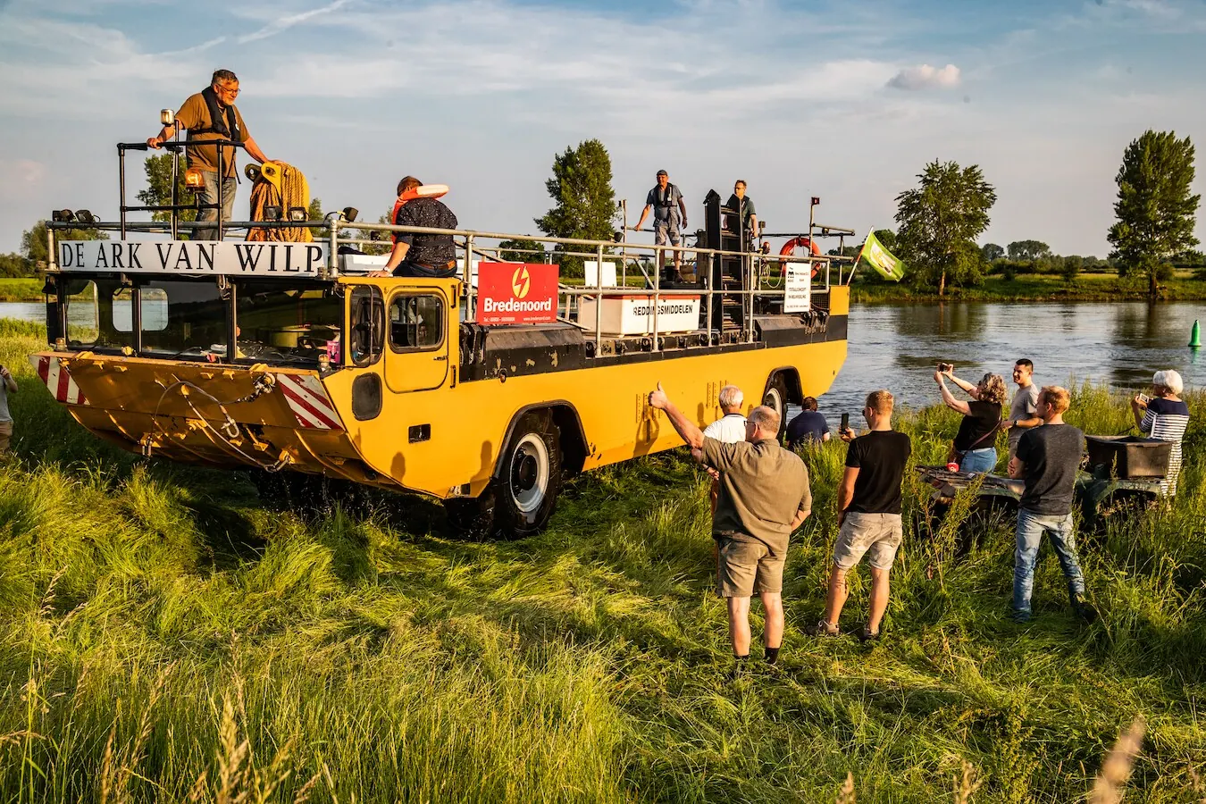 De Ark van Wilp met bemanning en belangstellenden aan de oever van de IJssel